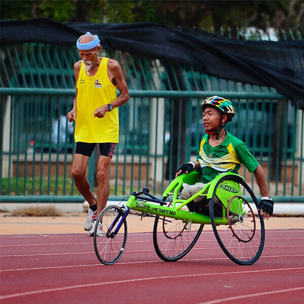 Wheelchair Athelete Running - Wheelchair Racing on Paralympic Track next to Elderly Man